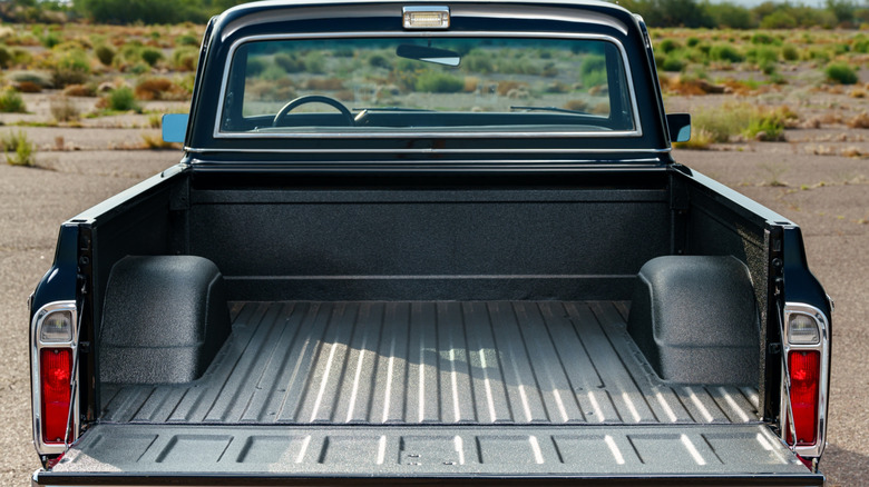Rear view of an empty pickup truck bed with wheel wells, tailgate down, and a desert landscape in the background.
