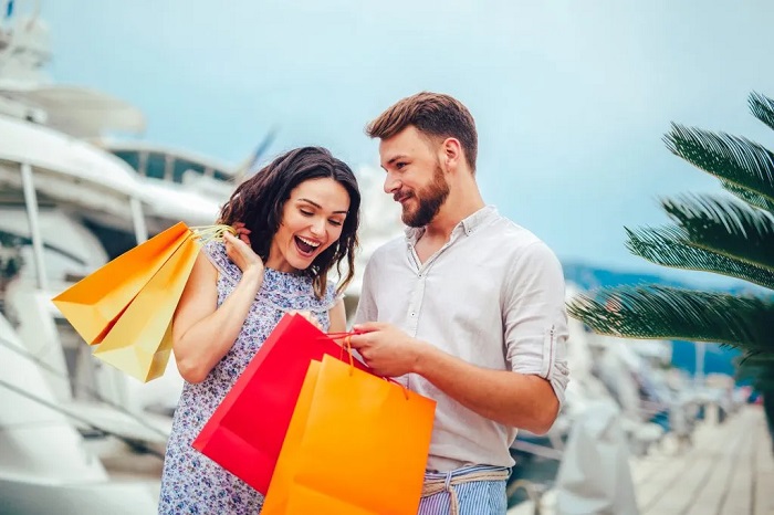 A smiling couple with colorful shopping bags beside a marina or waterfront.